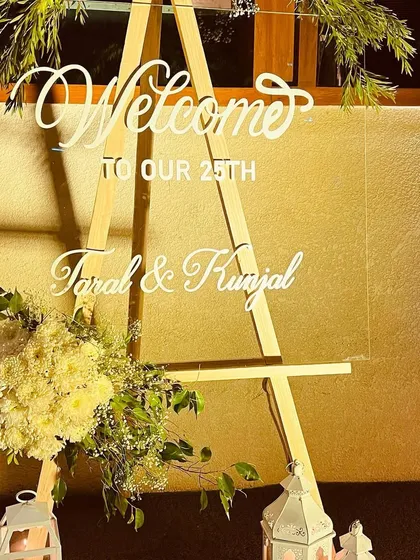 A personalized welcome easel for a 25th anniversary, featuring elegant white script and a beautiful floral arrangement.