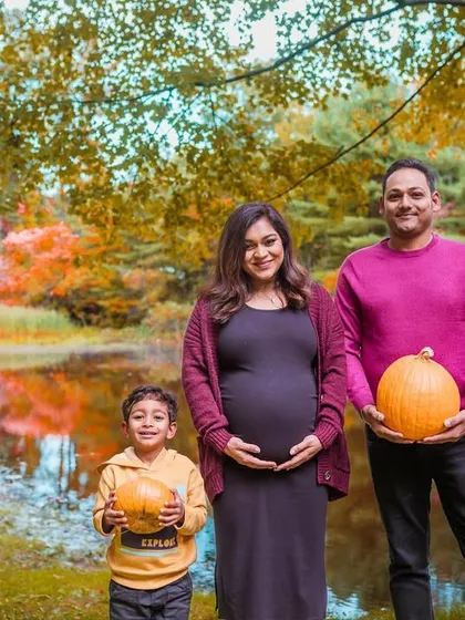 A festive fall family portrait. The family holds pumpkins against a backdrop of beautiful autumn foliage, perfectly capturing the seasonal spirit of their maternity shoot.