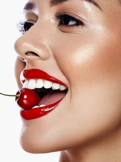 A moment of pure joy and vibrant color. This high-key beauty shot, with its glossy red lips and playful cherry prop, is designed for commercial appeal. It captures a feeling of fresh, confident energy that is perfect for a cosmetics campaign.