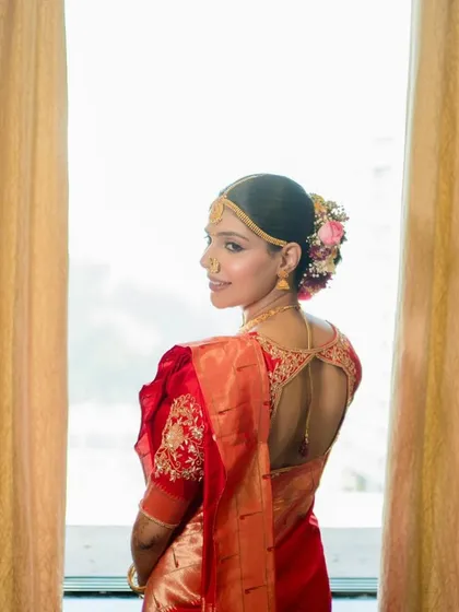 A beautiful back profile of my Maharashtrian bride, showcasing a traditional bun decorated with a mix of pink and white flowers, perfectly complementing her red saree.