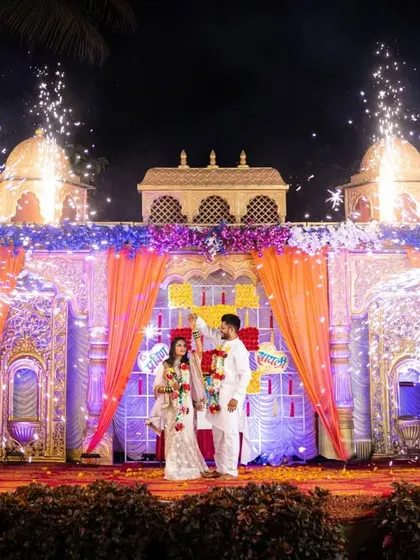 A grand Varmala stage with a palace-like backdrop and fireworks. This shot captures the magnificent scale of the wedding.