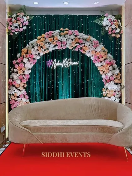 A custom neon hashtag is the centerpiece of this modern stage, framed by a beautiful floral arch against a dark green velvet curtain.