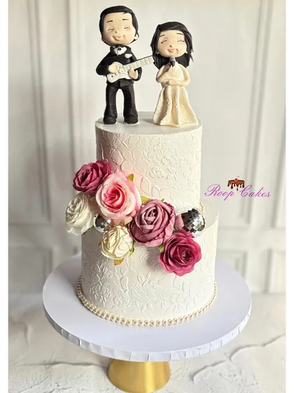 Celebrating a new beginning with a cake that tells a story. For this sangeet ceremony, I created custom fondant figurines of the couple as singers, complete with a guitar, set against an elegant, white-stenciled two-tier cake.