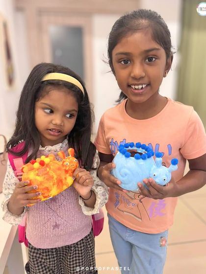 Two sisters proudly show off their finished painted planters, one a fiery snail and the other a cool blue one.