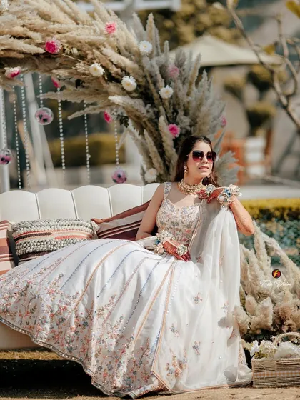 A relaxed portrait of the bride seated on a couch at her Mehendi, her elegant white lehenga and the pampas grass decor creating a chic, bohemian vibe.