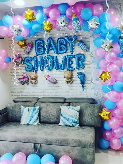 A lovely baby shower decoration designed around a sofa, creating a comfortable and festive spot for the mom-to-be. The arch of pink and blue balloons is accented with star and baby-themed foils.