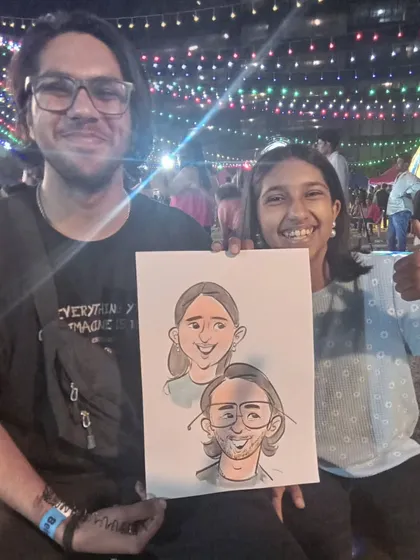 A couple's caricature drawn at an outdoor evening event. The festive lights in the background add to the magical atmosphere.