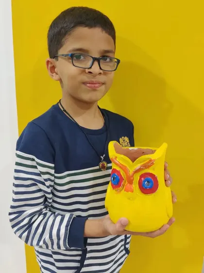 A young boy displays his finished yellow owl planter, a creative souvenir from a fun birthday celebration.