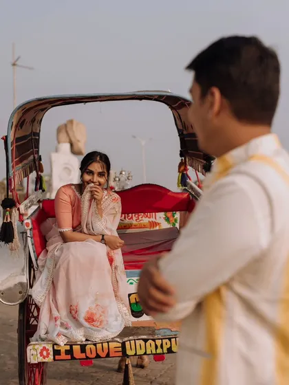A playful, over-the-shoulder shot capturing the bride's shy smile as she sits in a colorful rickshaw, with the words "I Love Udaipur" visible.