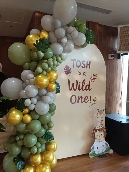 A closer look at the "Wild One" arched backdrop and balloon garland. The combination of muted greens, greys, and chrome gold balloons creates a modern and stylish jungle vibe.