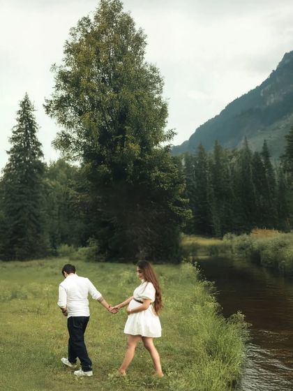 Walking together along the river. This shot captures the couple in motion, hand-in-hand, with the beautiful natural scenery of the forest and mountains creating a peaceful backdrop.