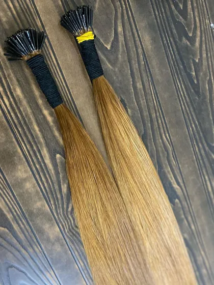 Golden blonde I-Tip extensions laid out on a wooden surface, highlighting their smooth texture and vibrant color.