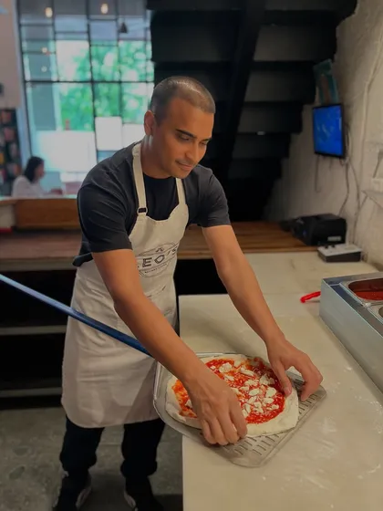 Gently sliding a pizza onto the peel. Every movement is careful and deliberate to maintain the perfect shape and structure.