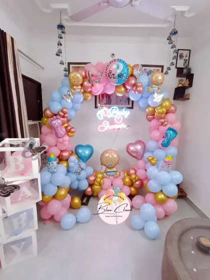 A full room view of a gender reveal baby shower, featuring a balloon ring, 'BABY' blocks, and butterfly accents.