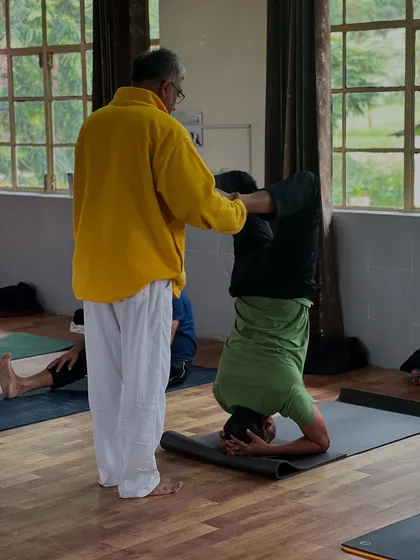 A teacher provides support to a student practicing a headstand variation. This hands on guidance is crucial for mastering advanced inversions safely.
