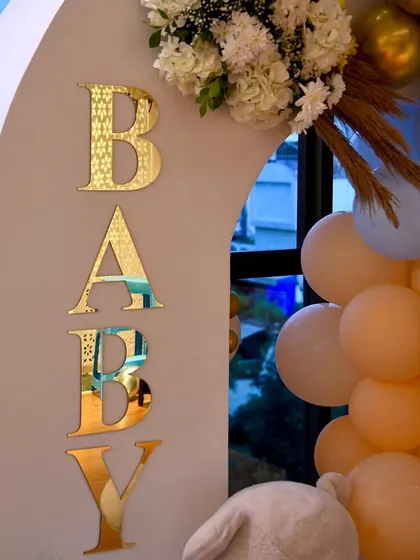 A close-up of the custom gold acrylic "BABY" letters on the welcome arch. The detailed pattern adds a touch of elegance.