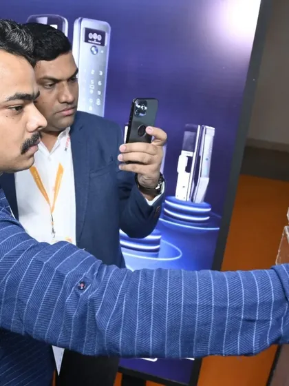 An attendee examines a smart door lock, while another captures the details on their phone. Our expo is a hub for both direct evaluation and digital content creation.