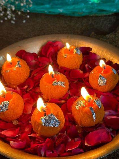 A bowl of my orange laddoo candles, all lit up. The flickering flames on the wax laddoos, nestled in a bed of rose petals, create a truly mesmerizing festive display.
