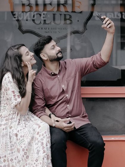 A fun, modern pre-wedding shot of a couple taking a selfie outside 'The Biere Club' in Bangalore.