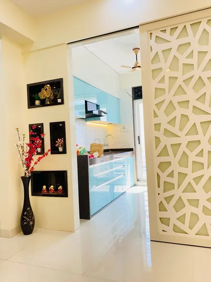 This view shows the transition from the living area to the kitchen, framed by a sliding jaali partition. The niche wall decor adds a personal touch to the space.