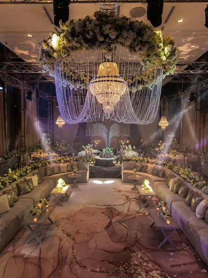 The gala night setup for a silver jubilee in Istanbul. A magnificent floral wreath and chandelier hang over a circular lounge seating, creating a space that is both grand and intimate.