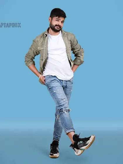 A full-body male model shot against a solid blue studio backdrop. The casual styling and relaxed pose create a friendly and approachable look for a commercial or lifestyle portfolio.