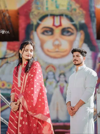 A unique and culturally rich portrait of a couple in traditional wear, posing in front of a vibrant mural of Lord Hanuman.