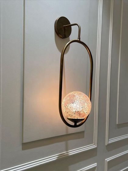 Detail of a custom-made wall light. The globe is crafted from stained glass mosaic, casting a warm, patterned light that adds a touch of artistry to the wall.