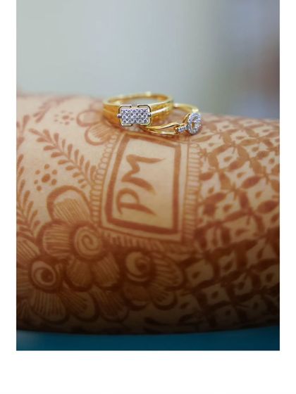 A close-up of the engagement rings resting on the bride's mehendi, which features the couple's initials.