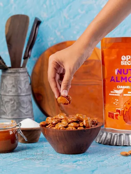 A lifestyle shot featuring caramel sea-salt almonds. Using a hand to pick up a nut creates a relatable moment for the viewer, making them want to reach in and grab one too.