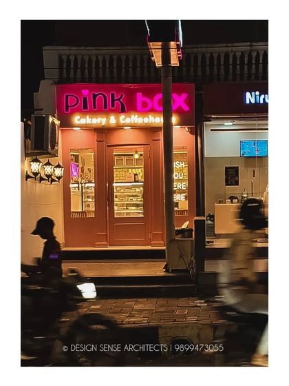The Pink Box bakery at night. The glowing pink sign and warm interior light create a beacon on the street, making it look like a charming, real-life dollhouse.
