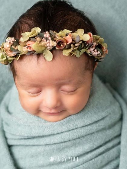 A close-up of a newborn's smiling face, framed by a delicate floral headband. These are the moments that make my heart melt.