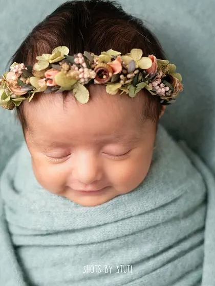 A close-up of a newborn's smiling face, framed by a delicate floral headband. These are the moments that make my heart melt.