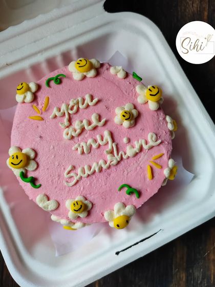 A bento cake that's pure sunshine. This pink cake is decorated with the message "You are my sunshine" and surrounded by adorable smiley-faced fondant flowers.
