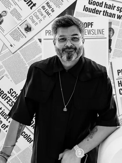 A professional portrait taken against a backdrop of Schwarzkopf Professional news clippings. A good headshot is part of representing yourself as a leader in the industry.