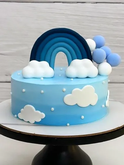 A beautiful blue ombre cream cake with a rainbow and fluffy fondant clouds. It feels like a perfect slice of a clear winter sky.