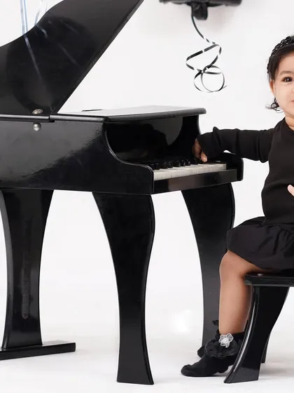 A little pianist in the making, this baby girl sits at a miniature grand piano for a unique and elegant first birthday portrait.