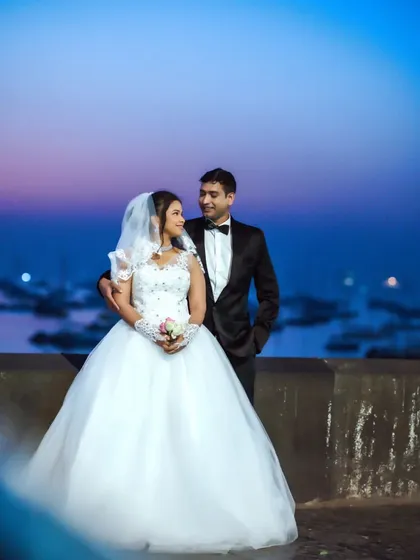 A stunning post-wedding or pre-wedding shoot with the couple in Christian wedding attire against a twilight sky over the Mumbai sea.
