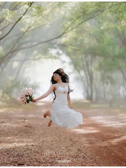 A joyful bride-to-be jumps in the air with a bouquet in hand, on a path surrounded by ethereal, misty trees. This shot is full of life and happiness.