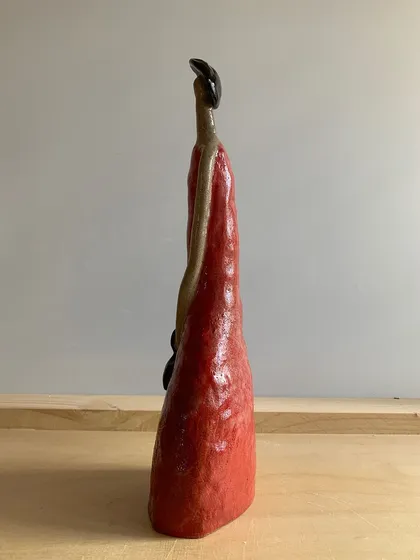 A side view of the 'Damn Red Woman' sculpture, showing her elegant, elongated form.