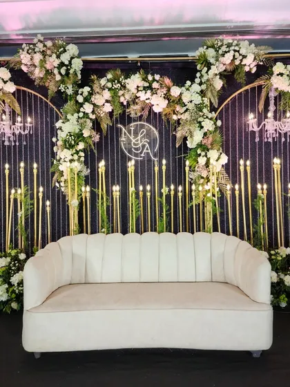 A close-up of the elegant couple's sofa against the candle-lit backdrop. The neon monogram adds a personal touch, while the cascading white flowers and mini chandeliers create a sense of luxury and romance.