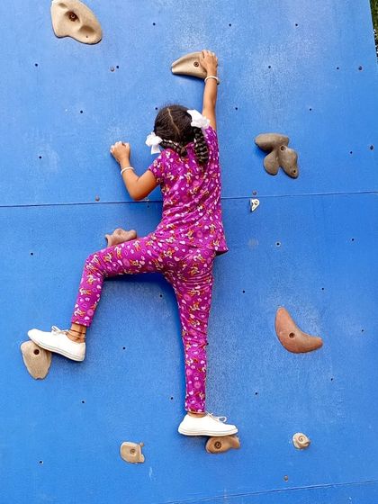 A young girl carefully makes her way up the artificial climbing wall, learning balance and coordination.