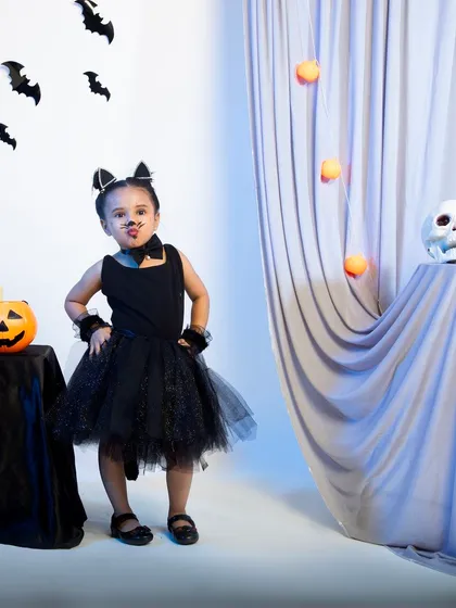 A child in a black cat costume making a cute face for the camera.