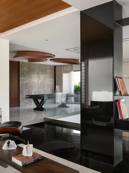 The interior spaces are designed for sophisticated leisure. This view shows the transition from a lounge area with an Eames chair to an entertainment zone with a pool table, unified by a palette of black marble and reflective surfaces.
