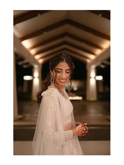 The bride, radiant in her shimmering sangeet outfit, sharing a quiet, happy smile before her performance.