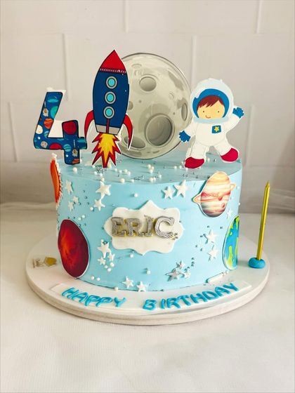 An adorable space-themed cake for a 4th birthday, with a rocket ship, astronaut, and planets.