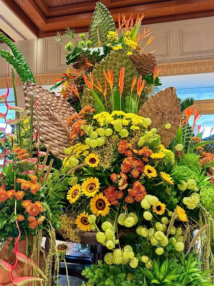 A detailed shot of a vibrant floral arrangement, highlighting the cheerful faces of sunflowers nestled among orange chrysanthemums and exotic greenery. I use woven natural textures to add another layer of rustic elegance to the design.