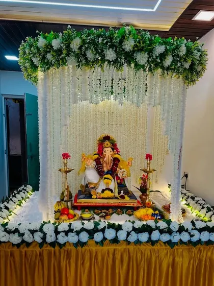 A variation of my popular canopy design, this mandap uses strings of white artificial flowers to create a beautiful curtain effect around the idol. The setup is framed with a lush arch of white and green florals.