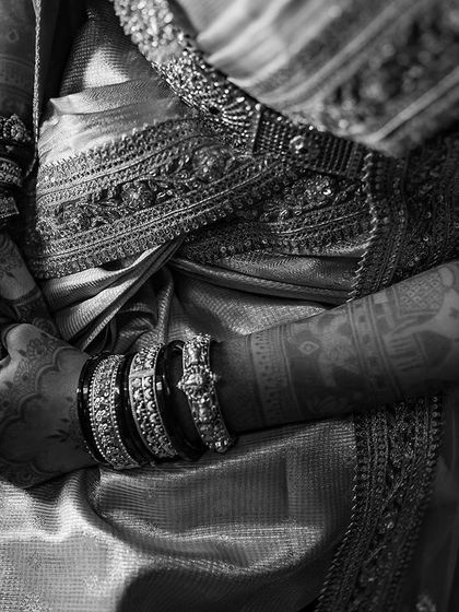 A black and white shot focusing on the bride's hands and the rich texture of her silk saree. The monochrome tones add a timeless, classic feel to the image.