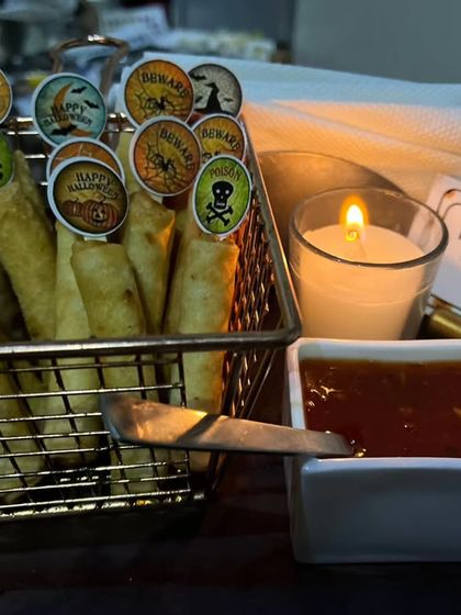 Crispy 'Finger Rolls' served in a wire basket with a blood-red dipping sauce. The Halloween-themed toppers with skulls and bats add a fun, spooky touch to this appetizer.